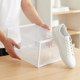 Caja ClearBox Fold sujeta entre las manos junto a una zapatilla para mostrar su tamaño